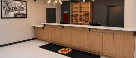 A reception area with a wooden counter, a black and yellow doormat, and a wall-mounted light fixture.