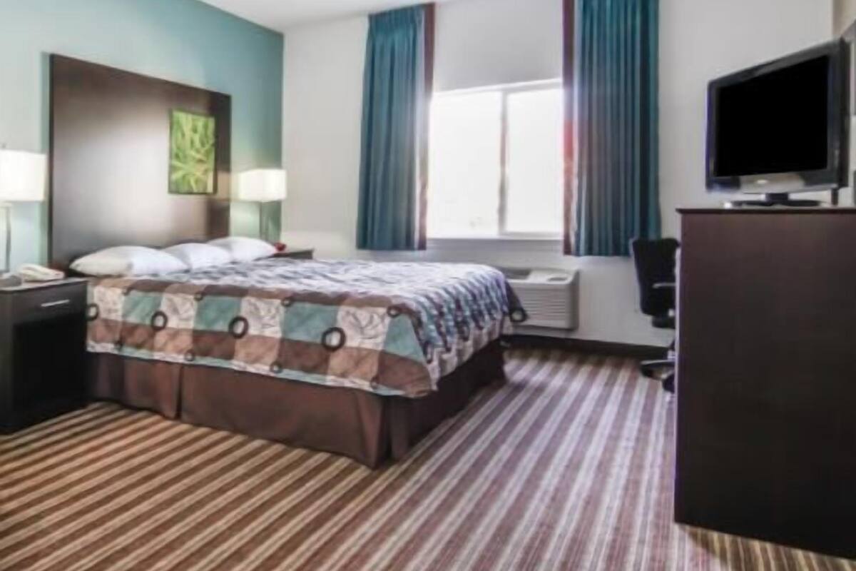 Une chambre d’hôtel avec un lit, un bureau, une télévision et une fenêtre avec des rideaux.