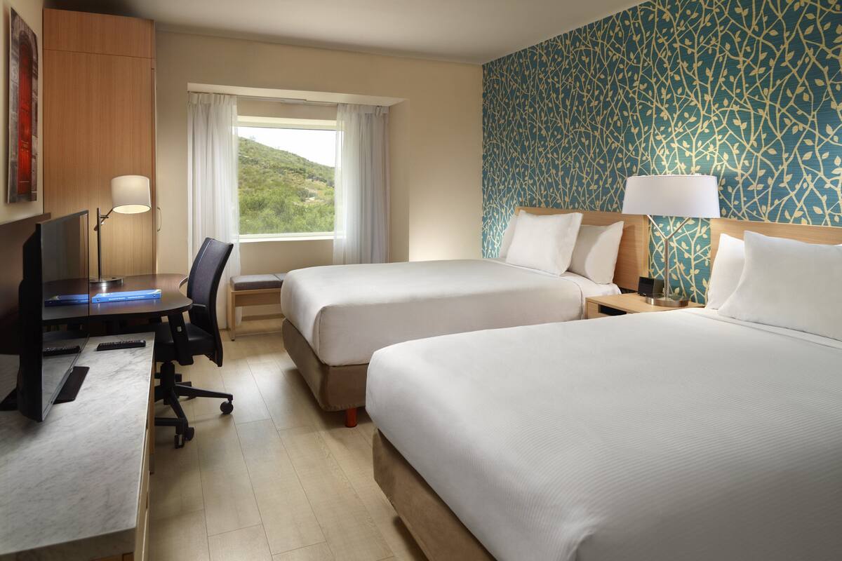 A hotel room with two beds, a desk with a computer, a chair, and a window with curtains.