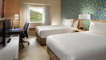 Una habitación de hotel con dos camas, un escritorio con computadora, una silla y un ventanal con cortinas.