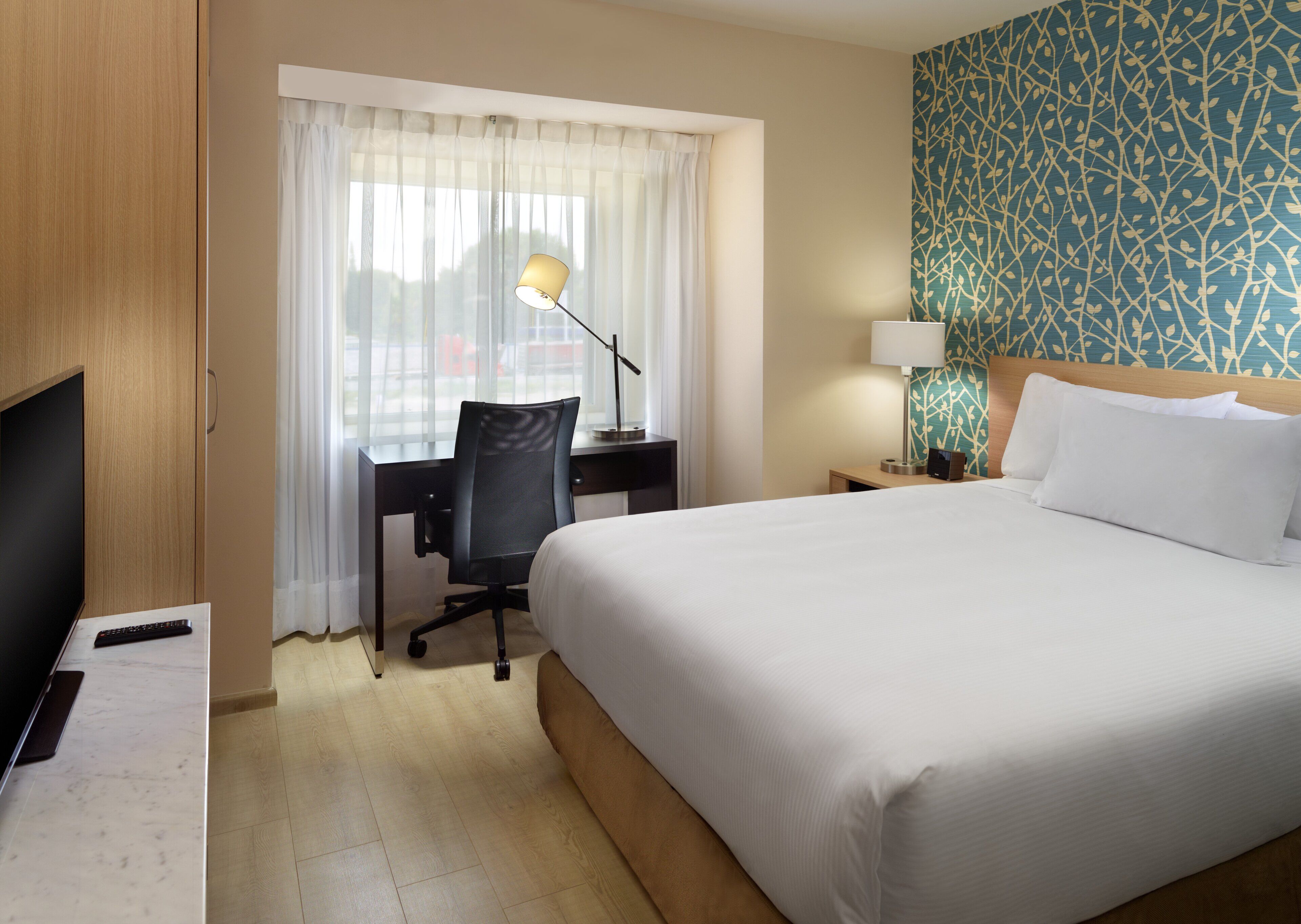 Una habitación de hotel con cama, escritorio, silla, televisor y cortinas.