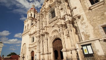 Un edificio histórico con arquitectura ornamentada, grandes puertas de madera y una imponente torre con campanas.