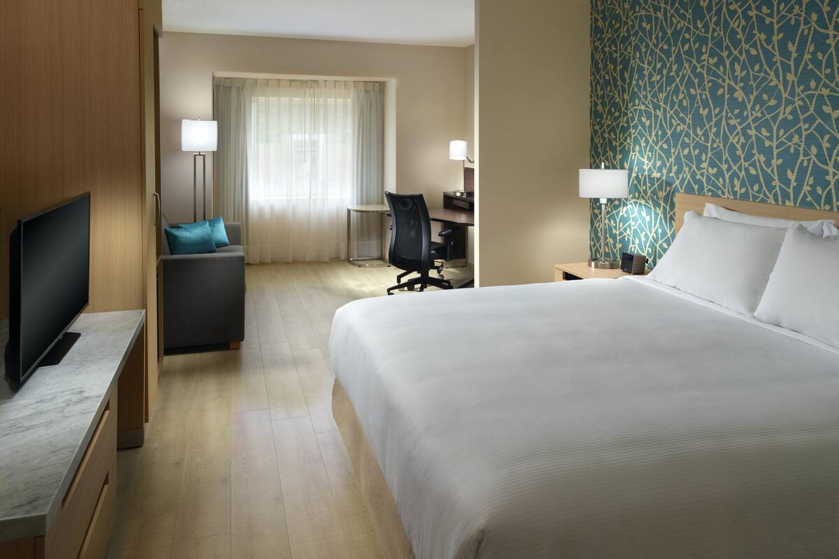 A hotel room with a large bed, a desk, a chair, a television, and a lamp.