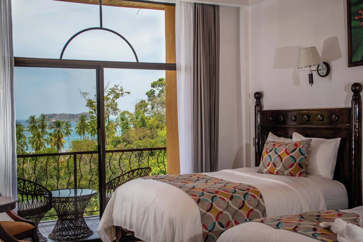 A hotel room with a large window offering a view of palm trees and the ocean.