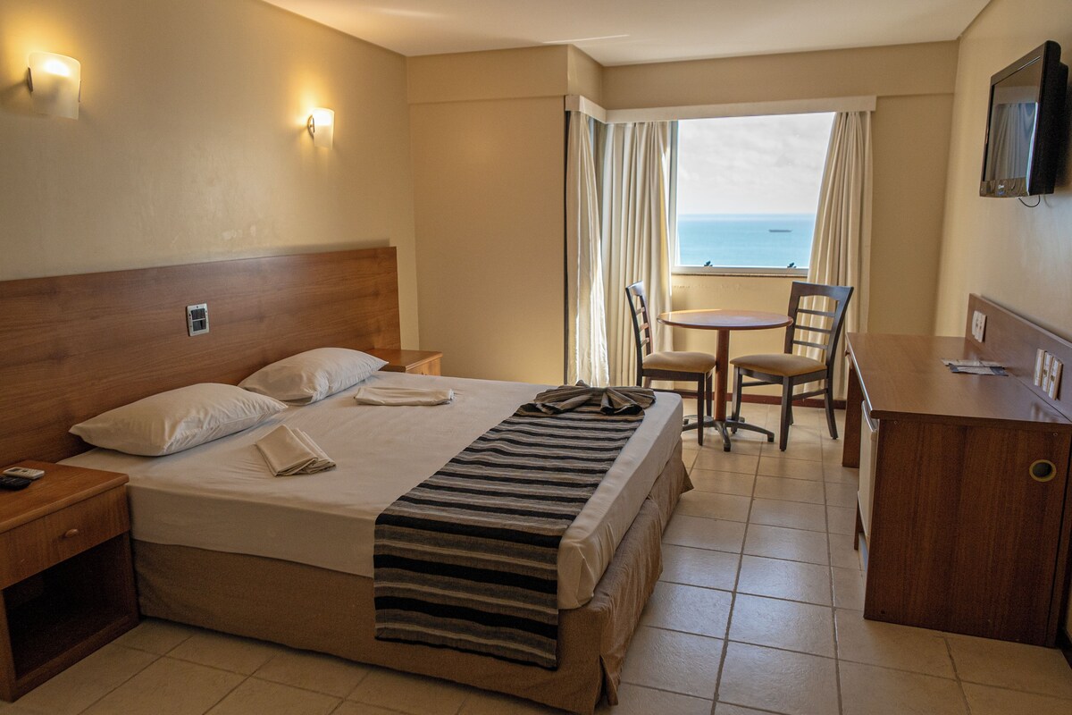 A hotel room with a bed, a desk, a chair, a TV, and a window with curtains.