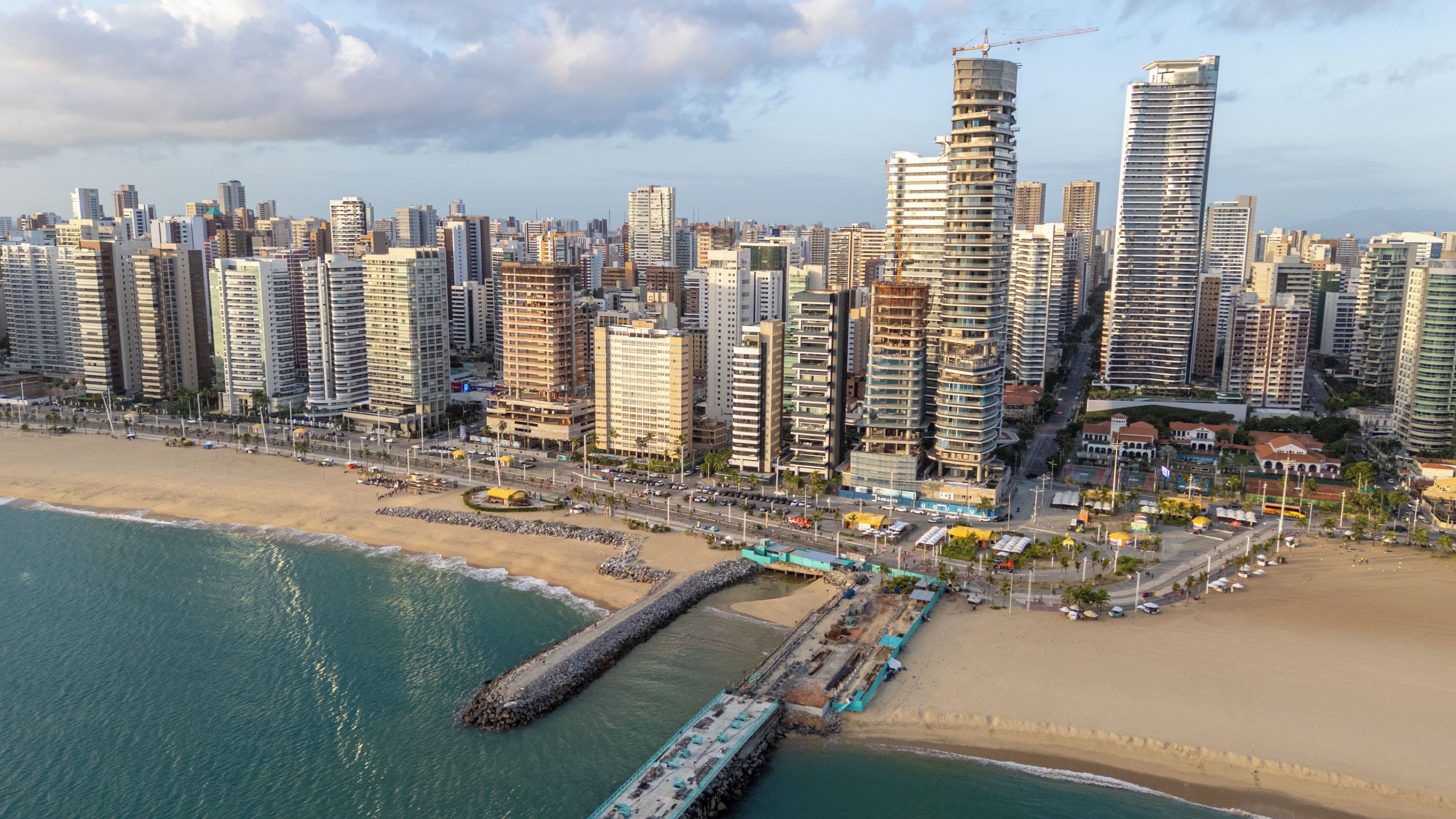 A coastal cityscape with high-rise buildings, a beach, and a pier.