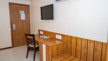A room with a wooden desk, a chair, a television mounted on the wall, and an air conditioning unit.