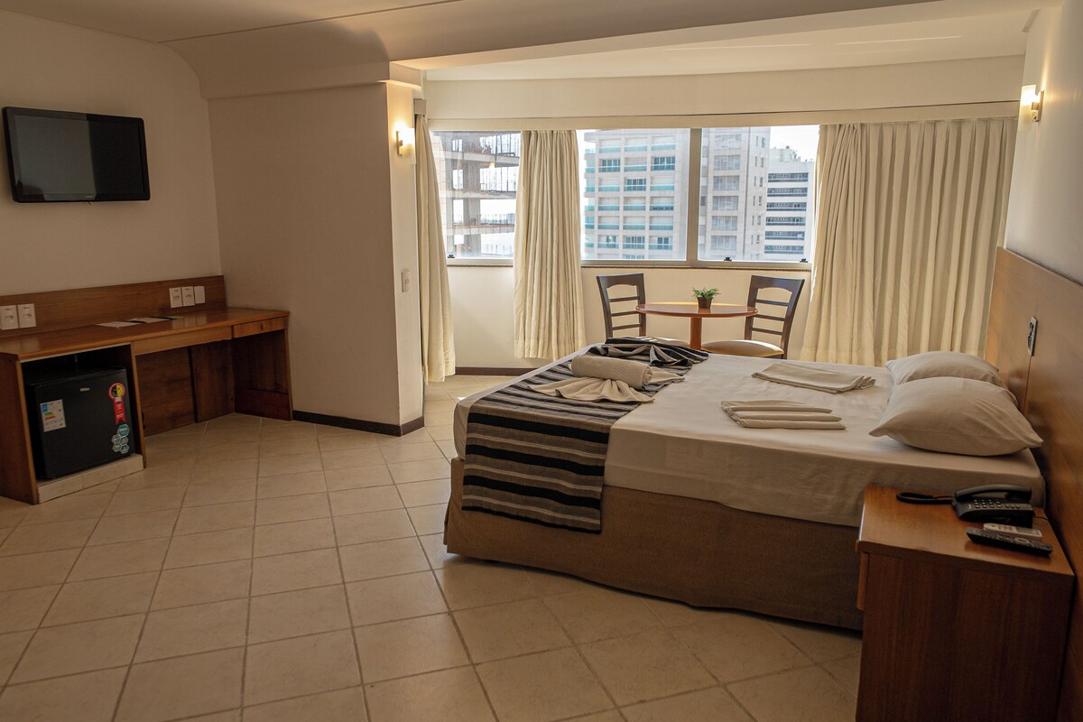 A hotel room with a bed, a desk, a chair, a TV, and a window with curtains.