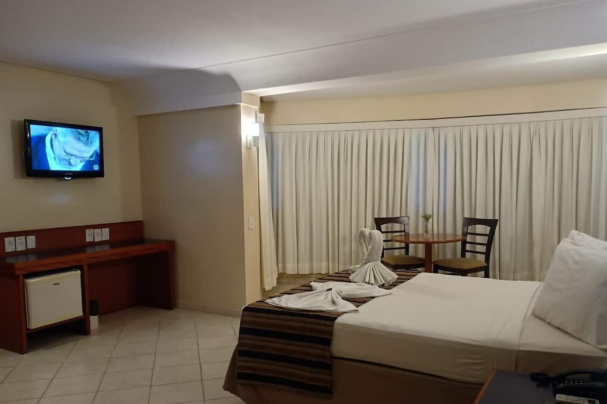 A hotel room with a bed, a desk, a television, and a window with curtains.