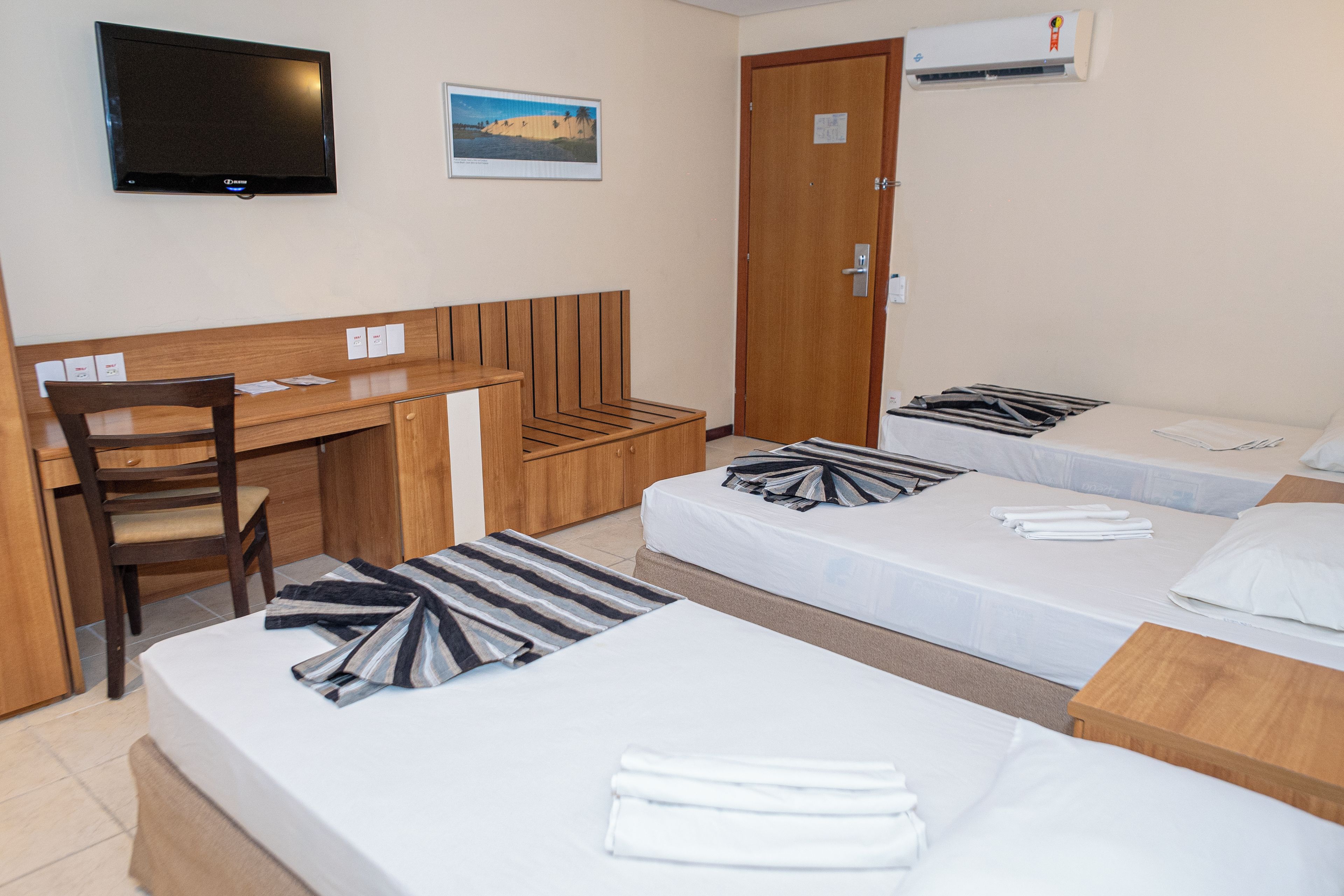 Une chambre d’hôtel équipée d’un bureau, de deux lits, d’une chaise et d’un téléviseur.
