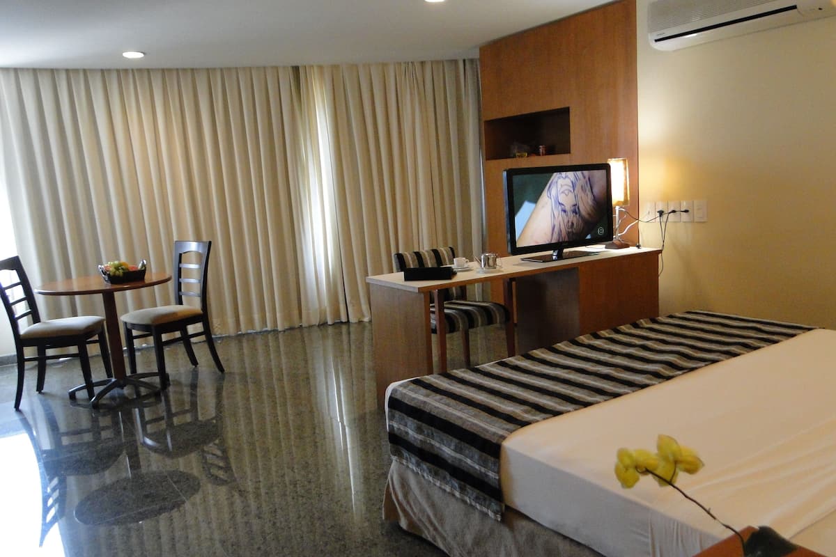 A hotel room with a bed, a desk, a television, a chair, and a table with a fruit bowl.
