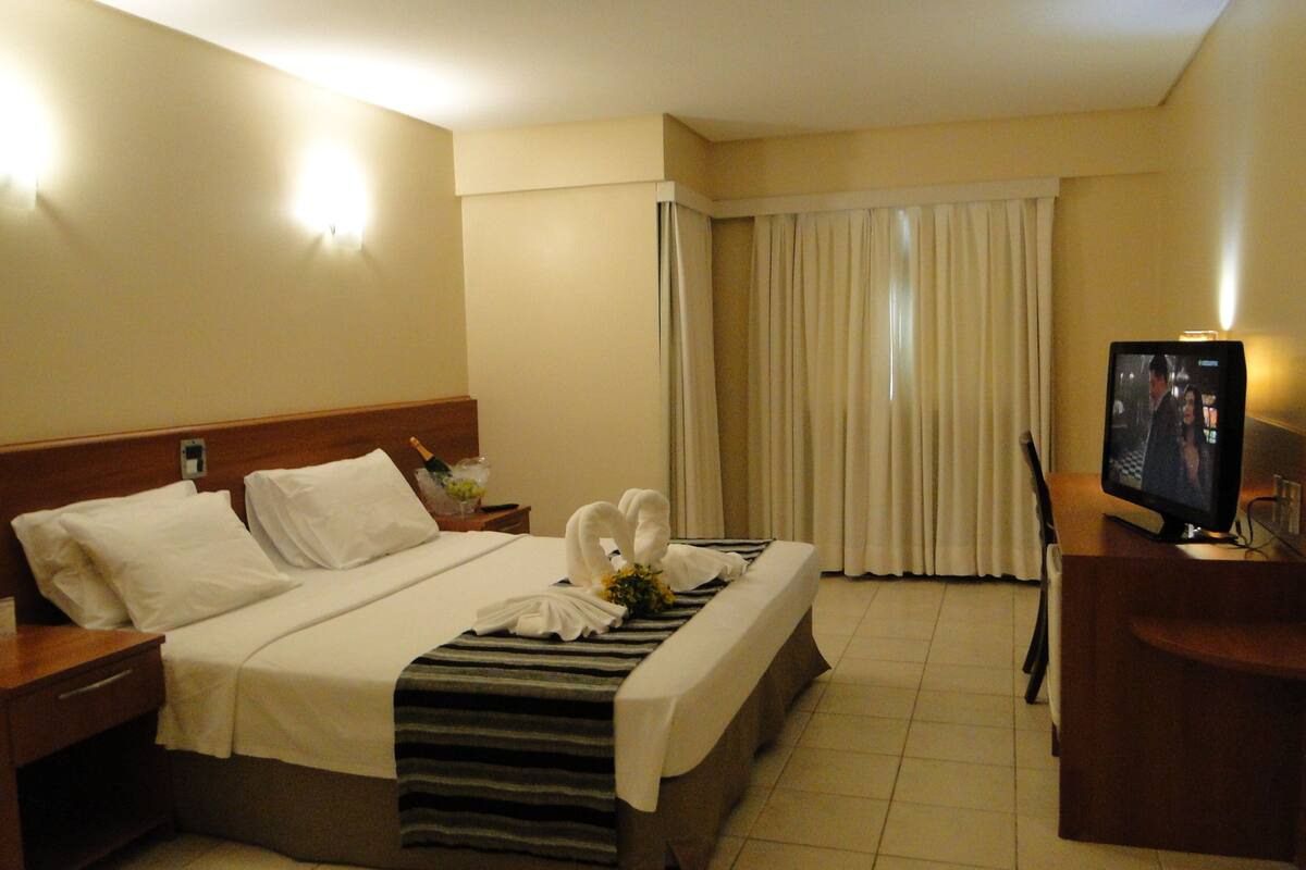 A hotel room with a bed, a desk with a television, and curtains.