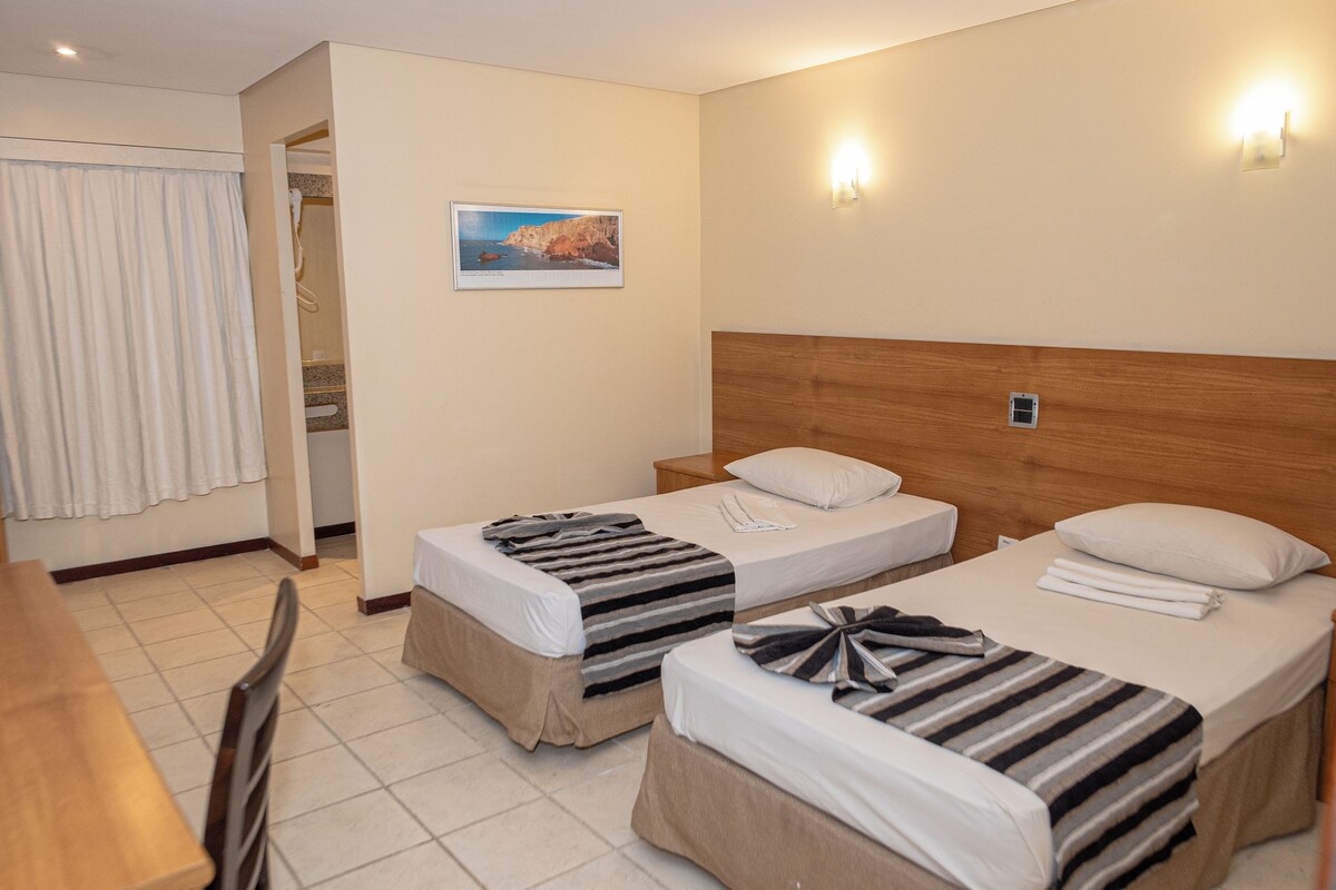 A hotel room with two beds, a wooden headboard, a painting on the wall, and a bathroom visible through an open door.
