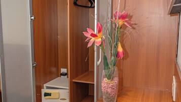 A hotel room with a wooden wardrobe, a desk with papers, and a vase with flowers.