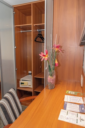 A hotel room with a wooden wardrobe, a desk with papers, and a vase with flowers. - Costa Do Mar Hotel (Fortaleza)
