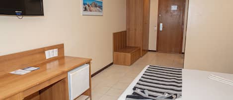 Une chambre d’hôtel avec un bureau en bois, un lit recouvert d’une couverture à rayures, un téléviseur fixé au mur et un tableau encadré au-dessus du bureau.