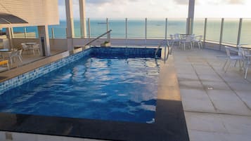Una piscina con vistas al mar, rodeada de asientos al aire libre y una terraza con baldosas.