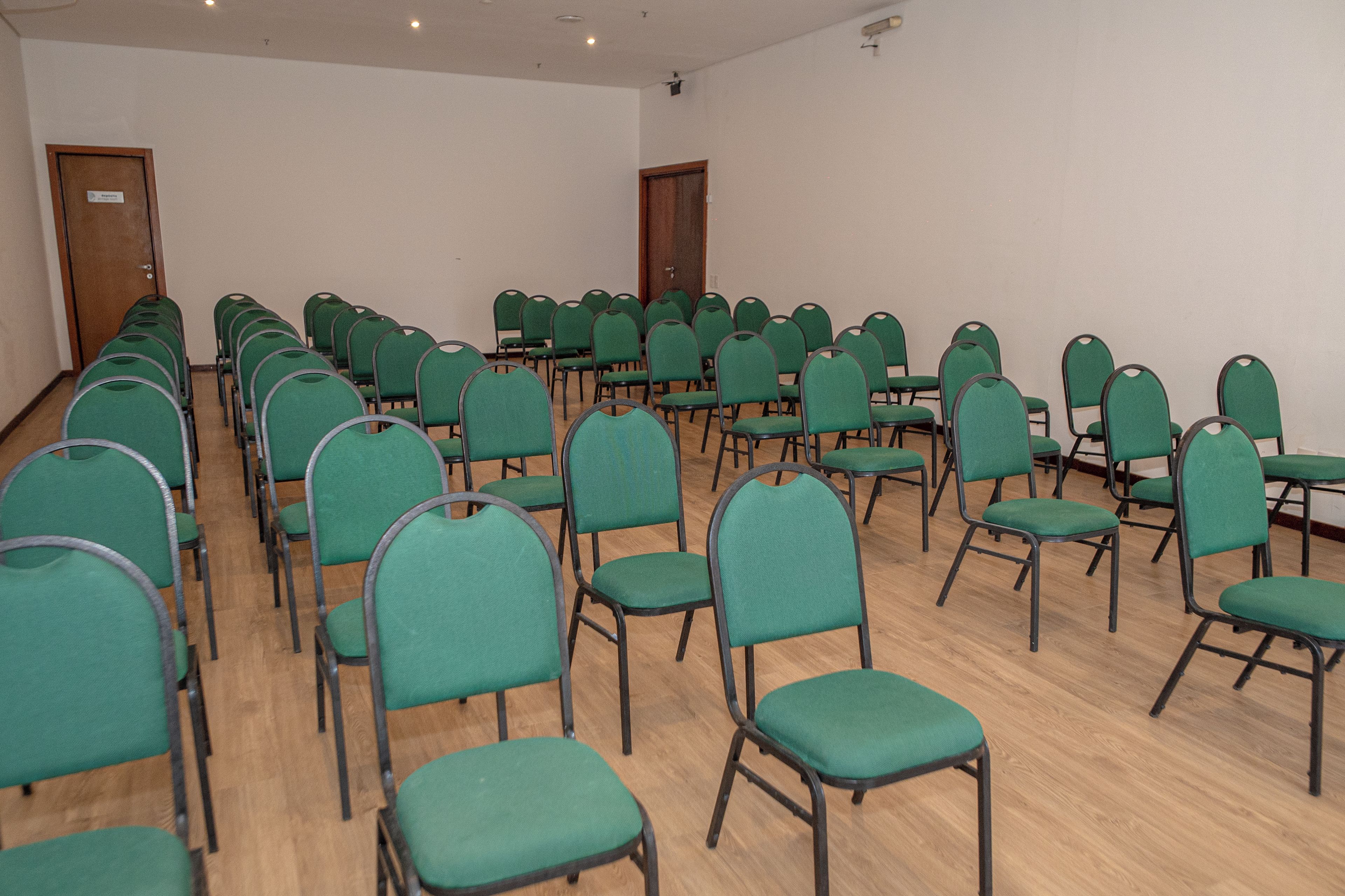 A conference room with rows of green chairs and wooden tables.