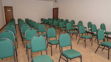A conference room with rows of green chairs and wooden tables.