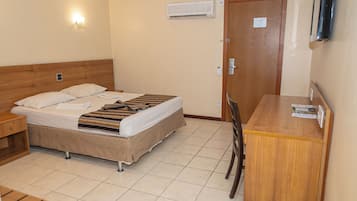 Habitación de hotel con cama, escritorio y silla. Hay un aire acondicionado de pared y una lámpara sobre la cama.