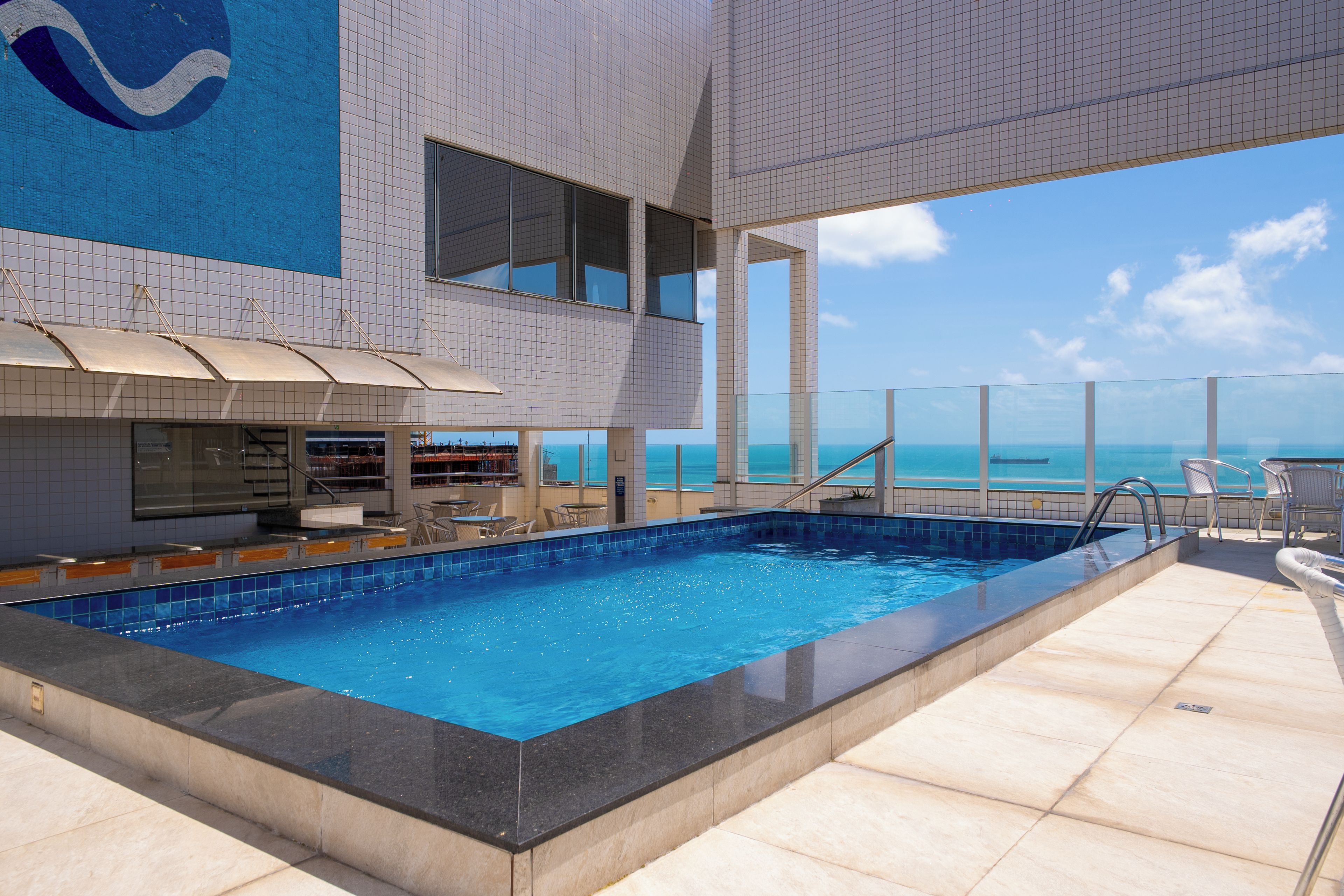 A rooftop pool with a view of the ocean, surrounded by lounge chairs and umbrellas.