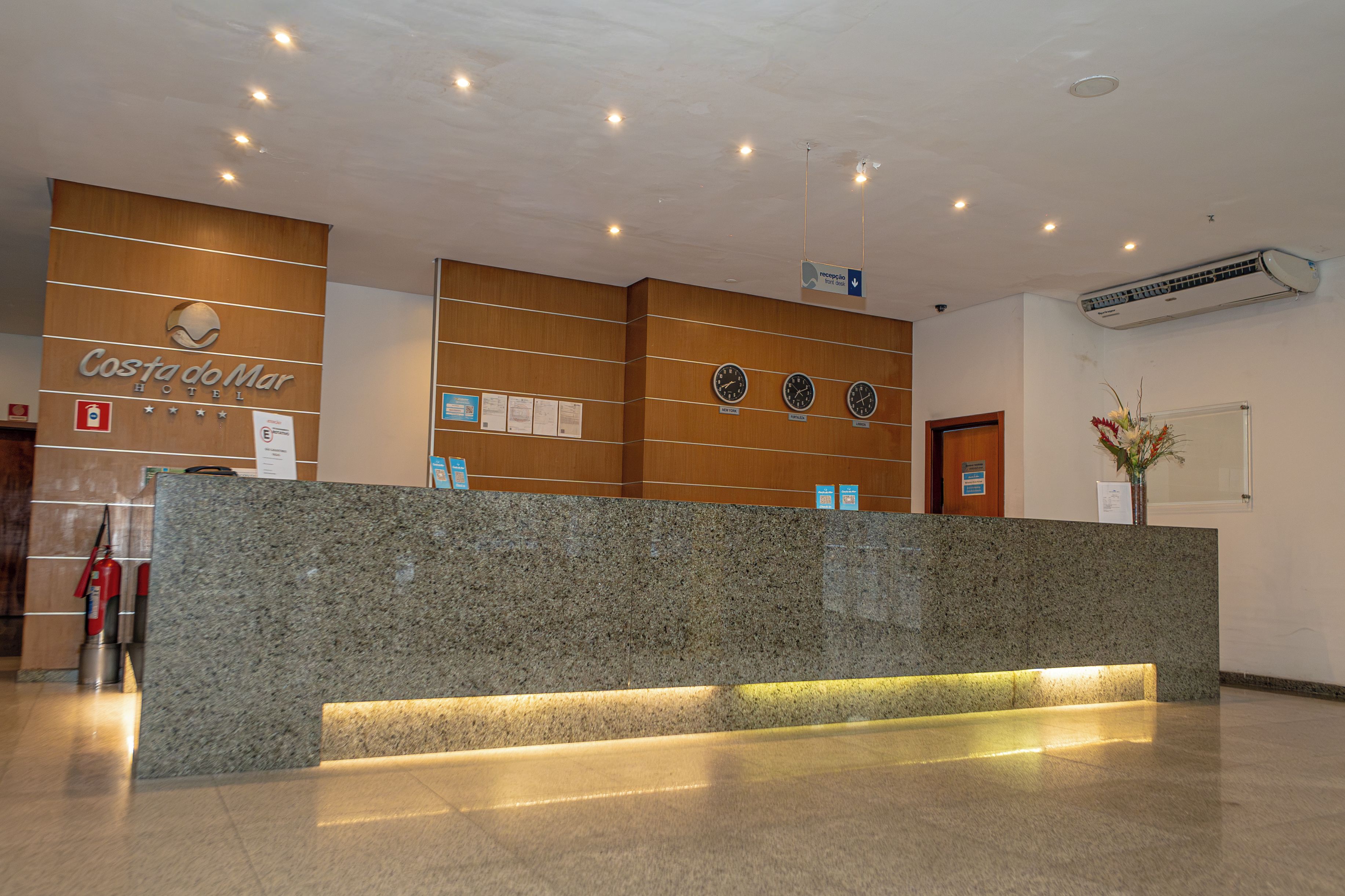A reception desk with a wooden panel design, a reception area with a clock, and a wall-mounted air conditioning unit.