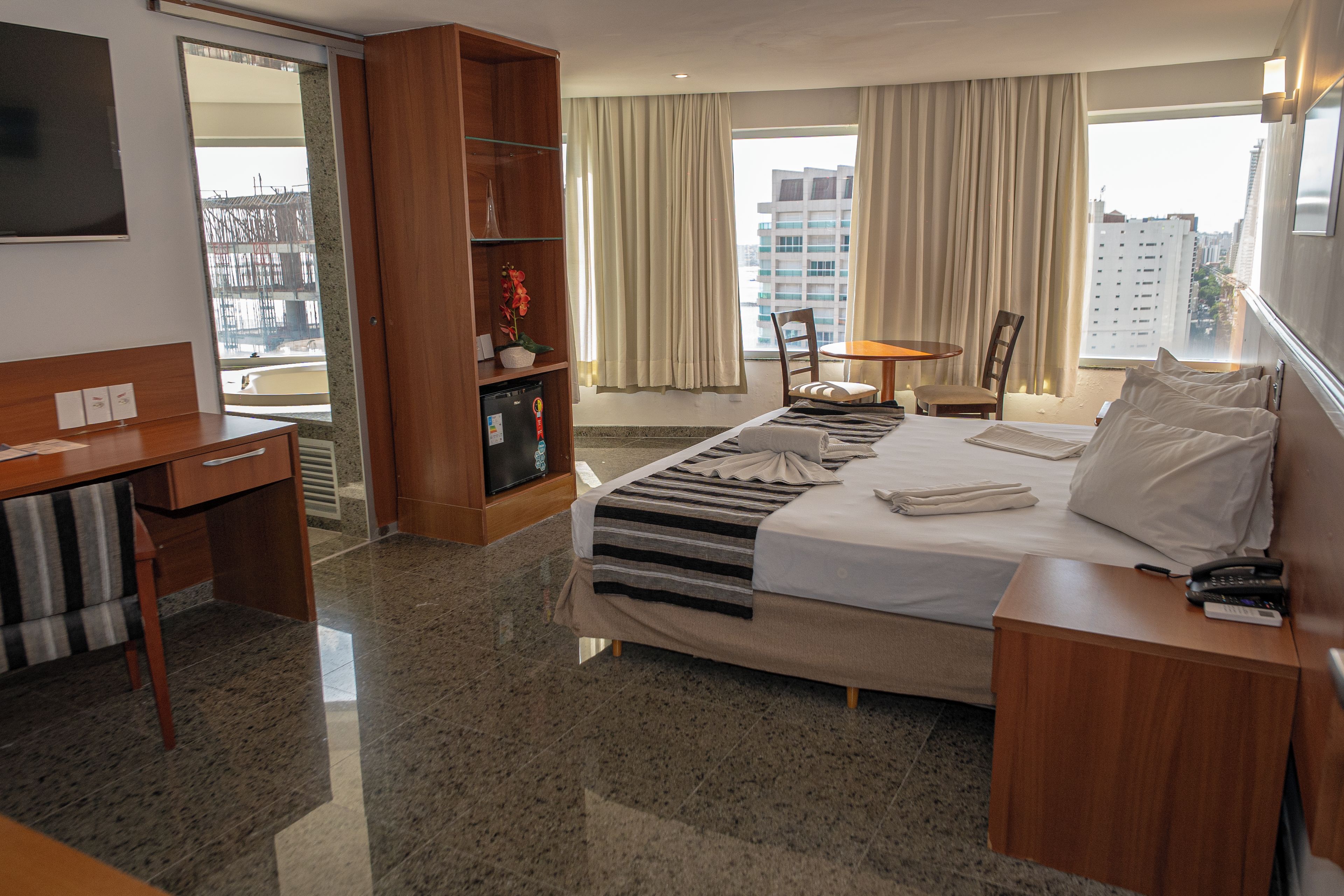 Habitación de hotel con cama, escritorio, estantería, silla y vista a la ciudad.