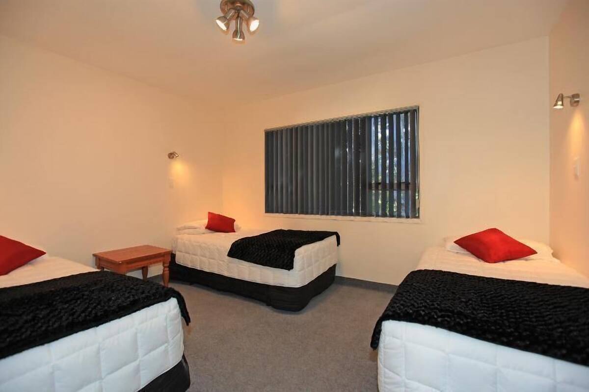 Ein Hotelzimmer mit zwei Betten, einem kleinen Tisch und einem Fenster mit Jalousien.