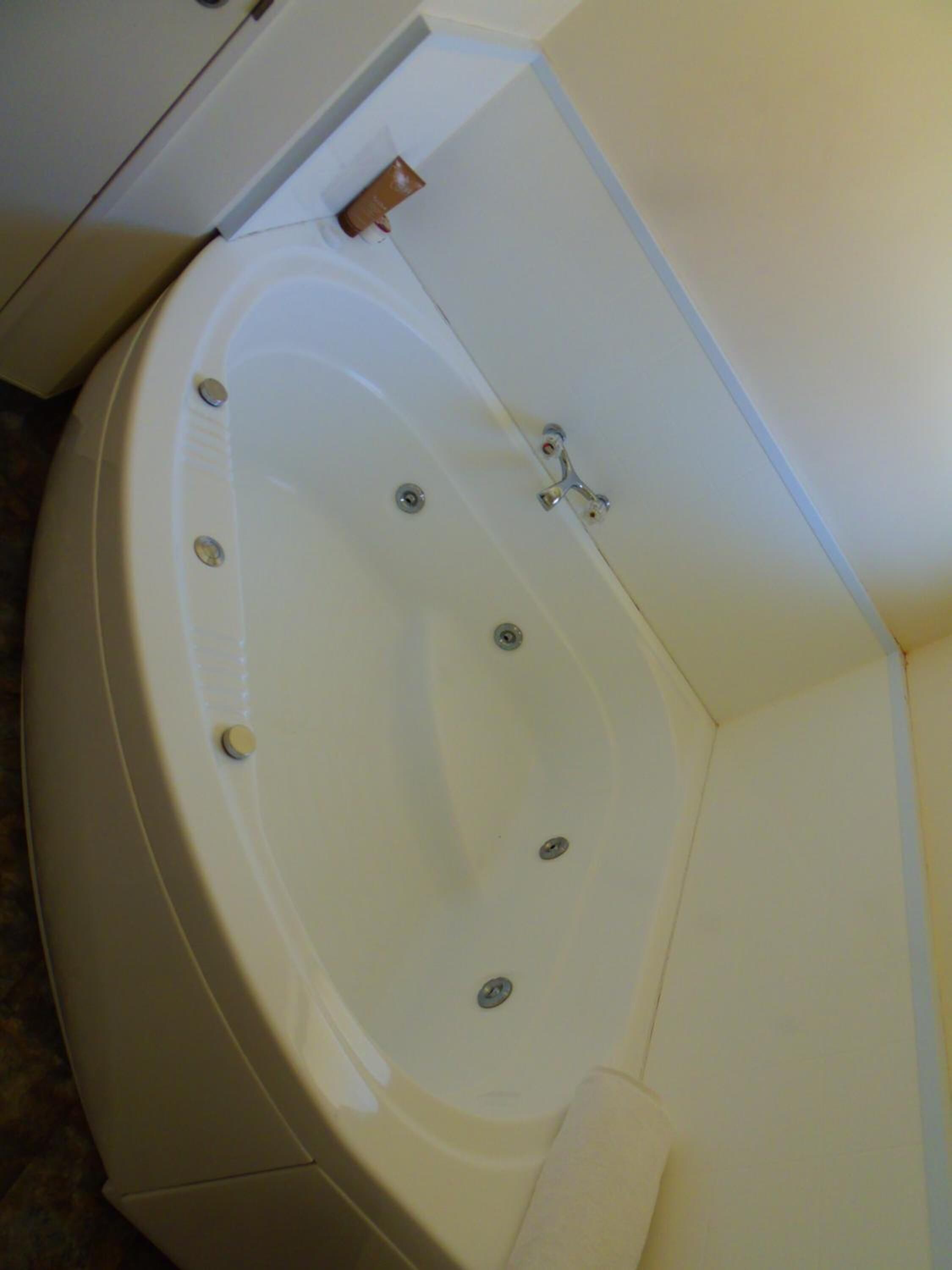 A corner bathtub with a wooden side panel, a towel, and a faucet.