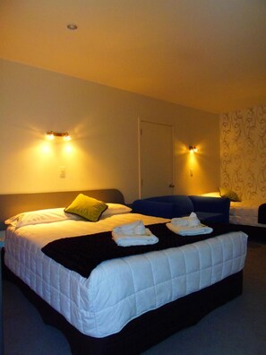 A hotel room with two beds, a dark-colored sofa, and a door. - Kapiti Lindale Motel & Conference Centre (Paraparaumu)