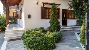 Un edificio con un camino de piedra, escalones de madera y un jardín bien cuidado con un alto árbol de hoja perenne.
