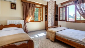 Una habitación con dos camas de madera, un pilar de ladrillo, una ventana con cortinas y un ventilador de techo.