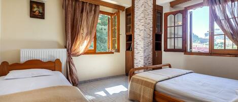 A room with two wooden beds, a brick pillar, a window with curtains, and a ceiling fan.
