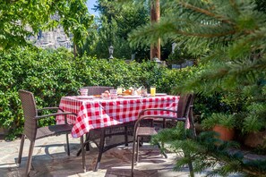 An outdoor patio with a checkered tablecloth, wicker chairs, and a potted plant. - San Giorgio Villa (Kalabaka)