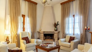 Un salón amplio con chimenea, asientos cómodos y ventanas grandes con cortinas.