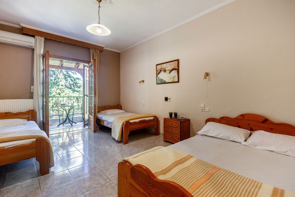 A hotel room with two beds, a wooden dresser, a small table, and a balcony with a view.