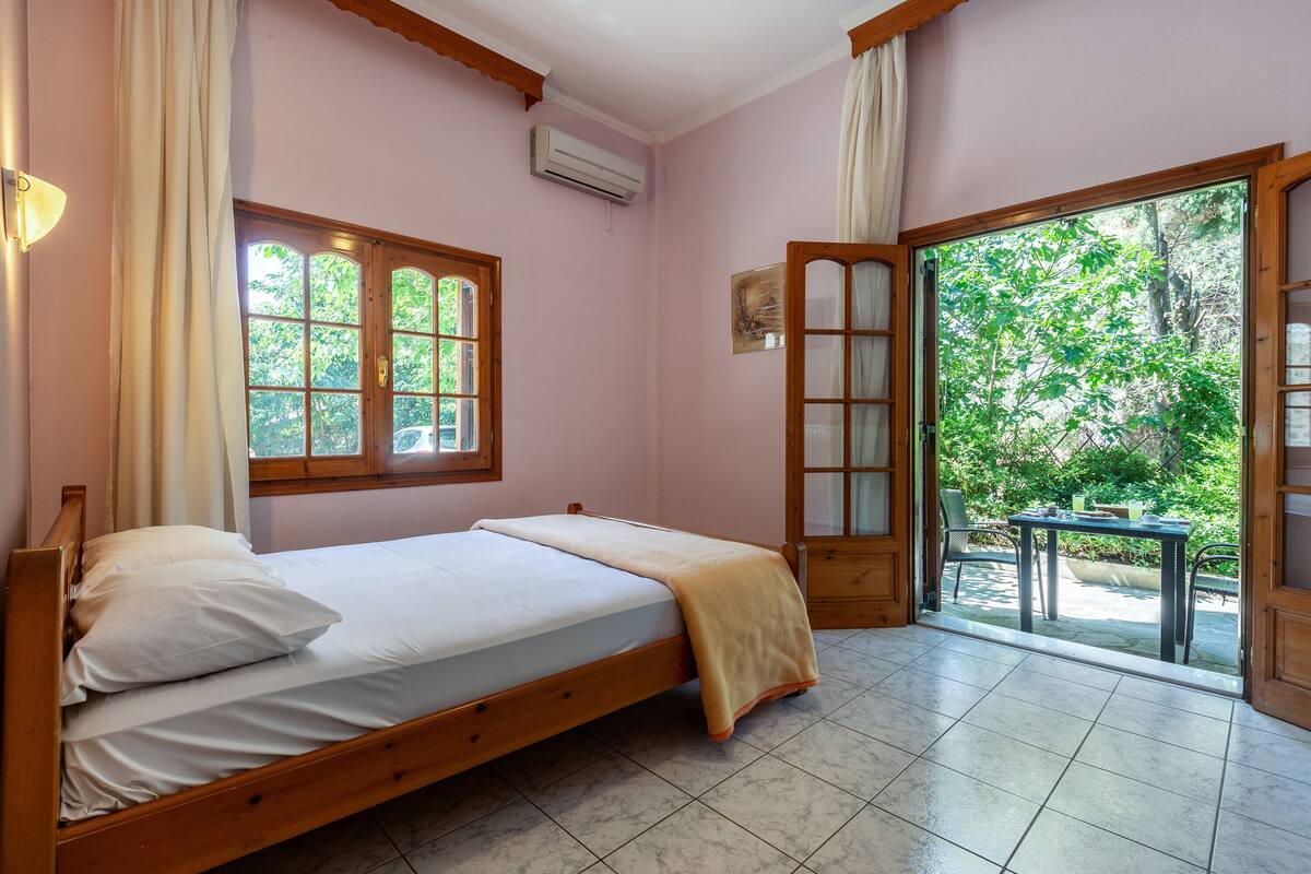 A bedroom with a wooden bed, a window, and a view of greenery outside.