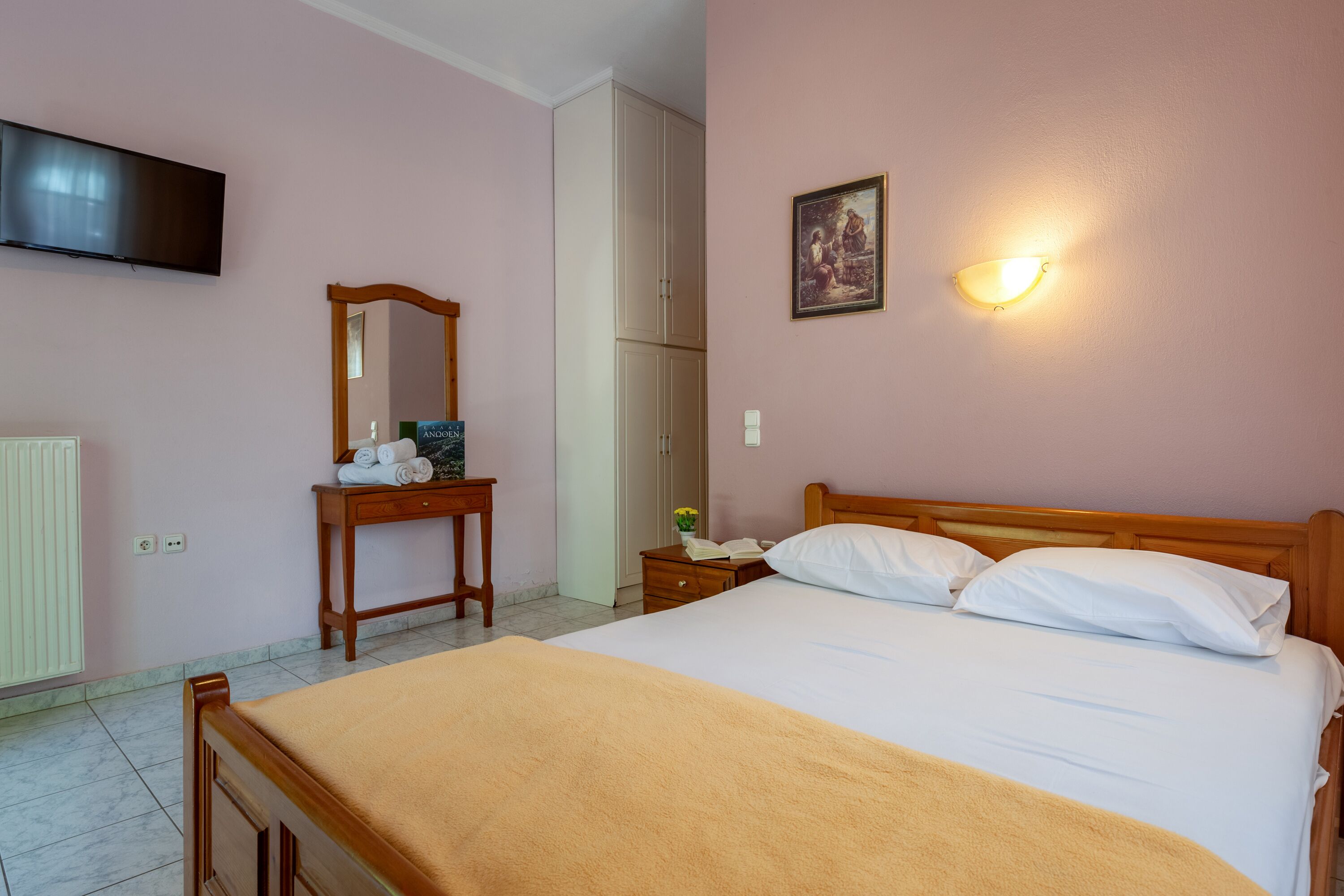 Une chambre à coucher comprenant un lit, une table de chevet, un miroir, un téléviseur fixé au mur et un luminaire fixé au mur.