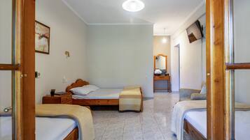 A hotel room with three single beds, a wooden headboard, a bedside table with a lamp, a small table with a plant, and a mirror on the wall.