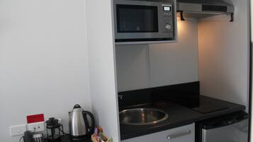 Uma cozinha compacta equipada com micro-ondas, chaleira, máquina de café e uma pia pequena.