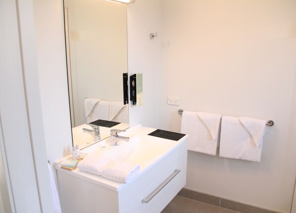 A bathroom with a white sink, two faucets, a mirror, and a towel rack with two towels. - ASURE Pukekura Motor Lodge (New Plymouth)