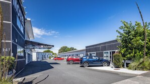 Un motel avec une entrée bien visible, un espace de stationnement couvert et une vue sur la rue où sont garées des voitures.