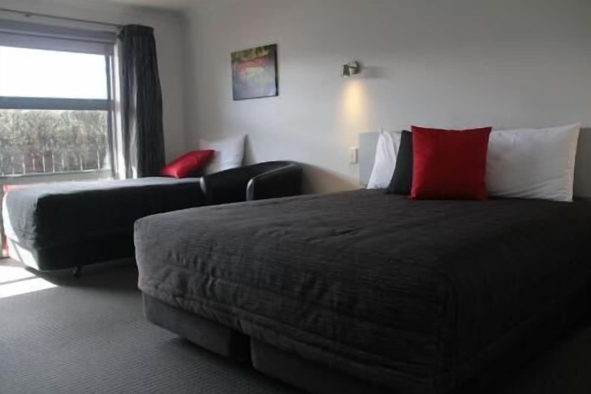 Habitación de hotel con una cama grande, un sofá más pequeño, una ventana con cortinas, una lámpara de pared y un cuadro.