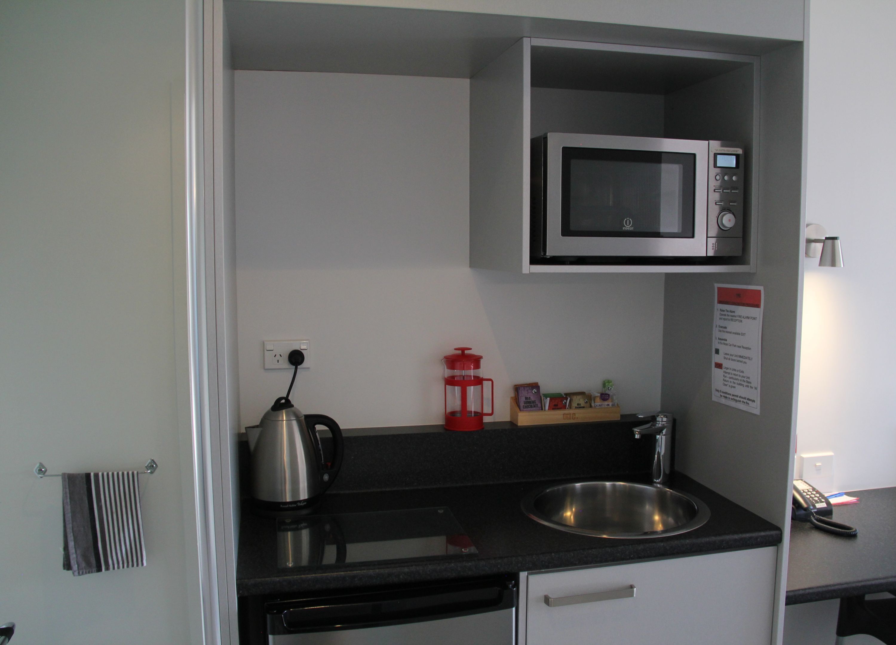 A compact kitchenette with a microwave, kettle, sink, and a small coffee maker.