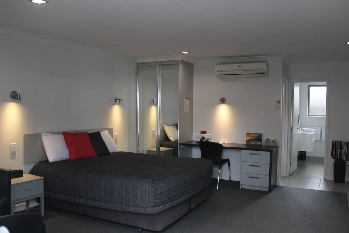 Una habitación de hotel moderna con una cama grande, un escritorio y una computadora. Hay un espejo, un armario y un equipo de aire acondicionado en la pared.