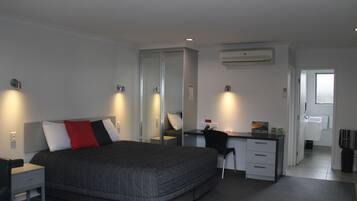 Une chambre d’hôtel moderne avec un grand lit, un bureau et un ordinateur. On y trouve un miroir, une armoire et un appareil de climatisation fixé au mur.
