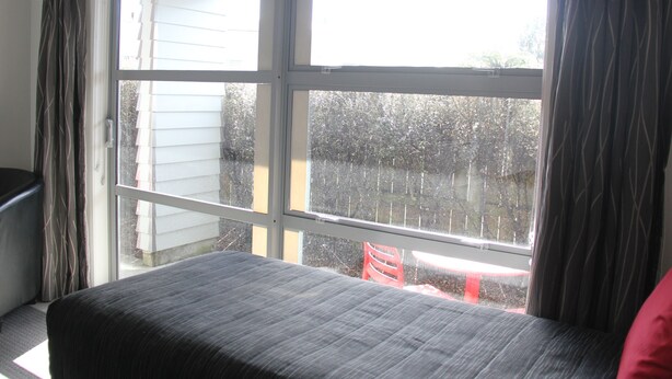 A room with a large window, a bed, and a red chair. - ASURE Pukekura Motor Lodge (New Plymouth)