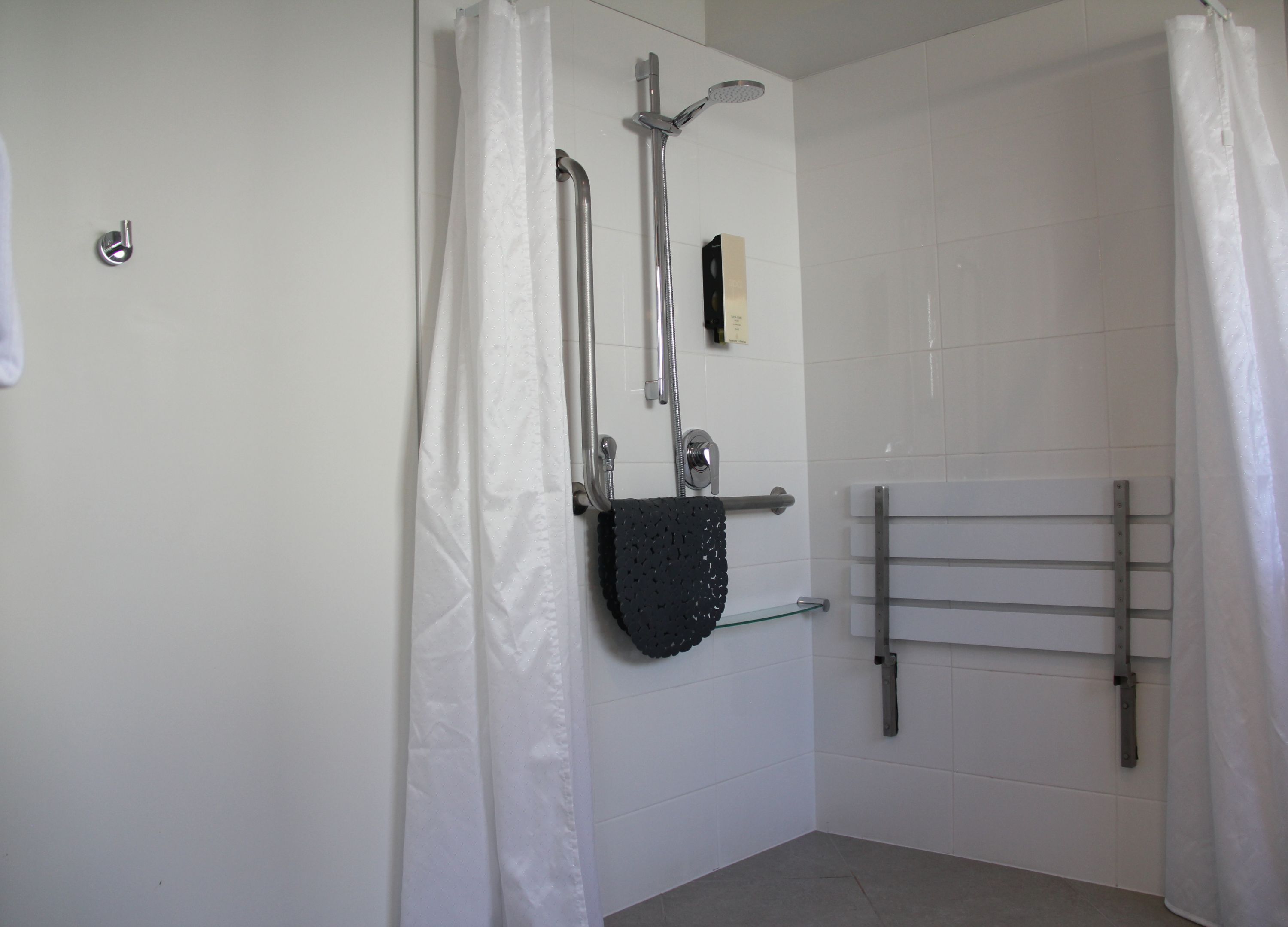 A bathroom with a shower, a towel rack, and a glass shelf.