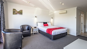 Une chambre d’hôtel avec un lit, une chaise, une table de chevet, un tableau au mur et une porte.