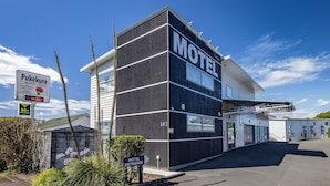 Un motel au design moderne, avec une enseigne « Motel » bien visible sur la façade, une entrée clairement identifiable et un espace de stationnement.